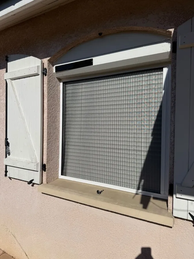Moustiquaire accordéon blanche posée sur une fenêtre à volets